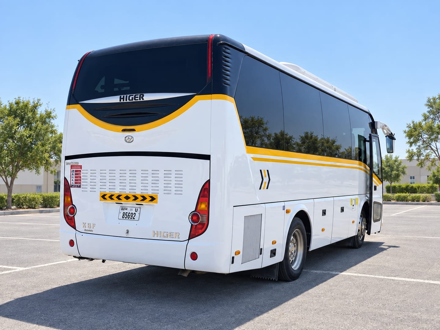 Rear three-quarter view of a white Higer coach with yellow side stripes