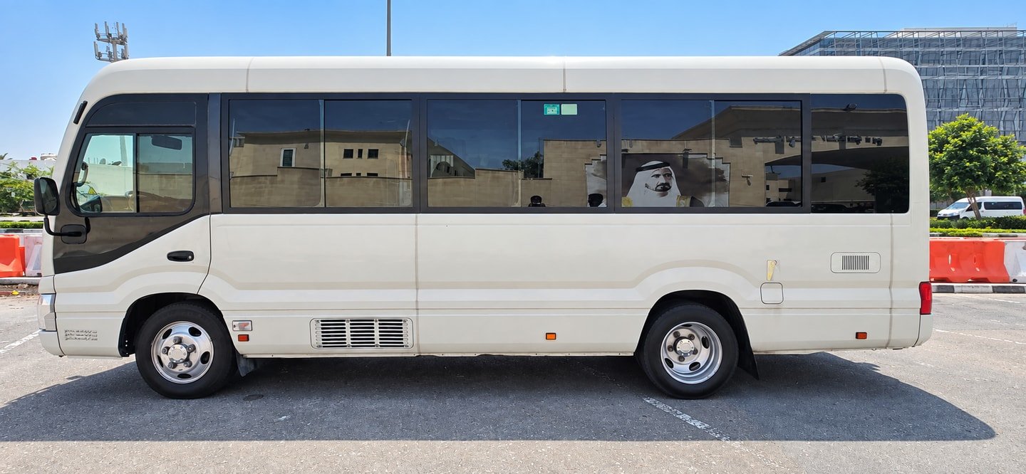 Side view of a white Toyota Coaster minibus with tinted passenger windows